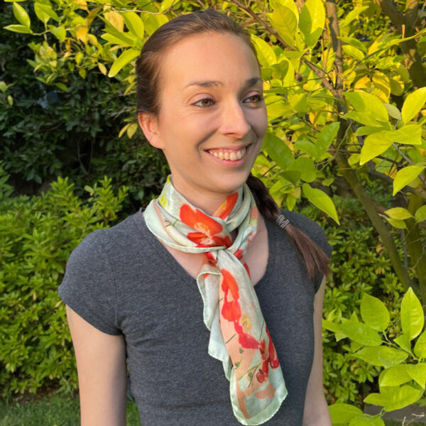 woman wearing a Petite long scarf in sea of poppies design, coral and sea foam colours tied at neck